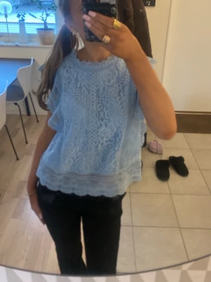 Ljusblå spetsblus med volanger. St L men är liten i storleken. - Söt ljusblå blus i spets med volangdetaljer och rund hals. Blusen har korta ärmar och ett romantiskt mönster i spetsen samt dekorativ kant nertill. Perfekt för dig som gillar en feminin och trendig stil.
