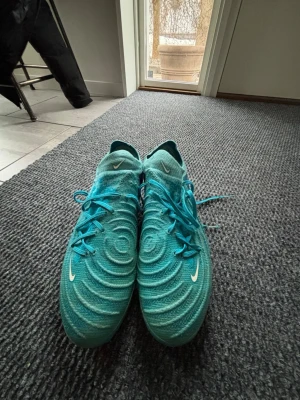 Turkosa Nike fotbollsskor med snörning - Säljer ett par turkosa Nike fotbollsskor med snyggt mönstrad ovandel och klassisk snörning. Skorna har en rund tå och är tillverkade i syntetmaterial för bästa prestanda på planen. Perfekta för dig som vill sticka ut på fotbollsplanen. Använda ett få antal gånger, inte använt dem sen förra vintern.