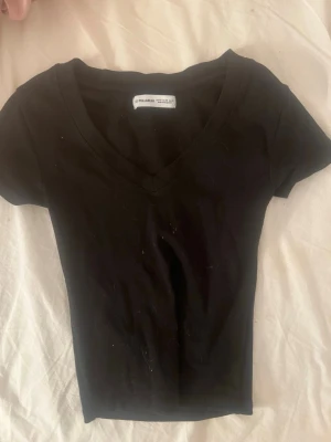 Svart v-ringad t-shirt från pull&bear - En enkel svart t-shirt från pull beat  med v-ringning och korta ärmar. Modellen är figurnära och passar perfekt till jeans eller kjol. Tillverkad i mjuk bomull för en bekväm känsla hela dagen.