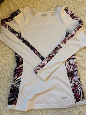 Vit långärmad träningströja ❣️ - Snygg vit långärmad träningströja från Stronger med färgglada paneler i lila, rosa och svart längs sidor och ärmar. Tillverkad i stretchigt funktionsmaterial som passar perfekt till gymmet 🩵