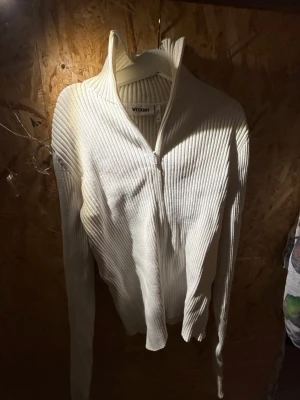 Vit ribbad ziptröja från Weekday - Snygg vit ribbad tröja från Weekday med dragkedja framtill och hög krage. Tröjan har lång ärm och är tillverkad i ett stretchigt material som sitter tajt. Perfekt för lager på lager och enkel att styla till olika outfits.