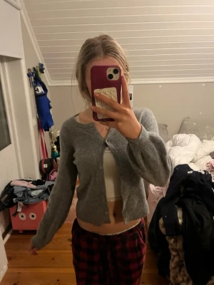 Grå kofta från Stockh lm - Mysig grå kofta från Stockh lm med rund halsringning och knäppning framtill. Koftan har långa ärmar och ribbade muddar vid ärmslut och nederkant. Perfekt att slänga över en topp för en chill look.