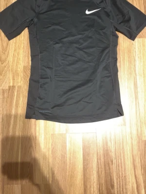 Svart Nike Pro Dri-Fit träningströja - Svart kortärmad träningströja från Nike Pro med Dri-Fit-teknologi som håller dig torr under träningen. Tight fit-modell med vit Nike-logga på bröstet och diskreta sömdetaljer längs sidorna. Perfekt för intensiva träningspass. Nästa. Aldrig använt den 