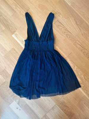 Marinblå kort klänning med v-ringning - Snygg marinblå kortklänning med djup v-ringning och breda axelband. Kjolen är lätt utställd och har ett tunt, svepande tyg. Perfekt för dig som gillar en stilren och ungdomlig look.