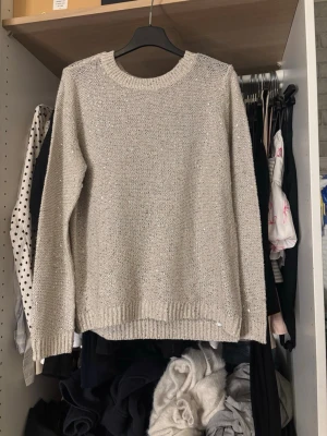 Beige stickad tröja med paljetter - Säljer en beige stickad tröja från Vero Moda i storlek L, men passar även S-M. Tröjan har rund halsringning, långa ärmar och är dekorerad med små silvriga paljetter som ger ett glittrigt intryck. Perfekt för dig som vill ha något extra till din vardagslook.