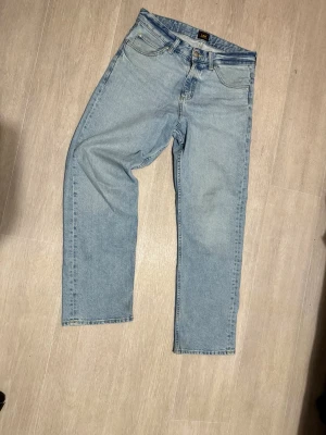 Ljusblå raka jeans från Lee - Säljer ett par klassiska ljusblå jeans från Lee med rak passform och fem fickor. Jeansen har en enkel design utan slitningar eller dekorationer och är tillverkade i mjukt denimtyg. Perfekta till vardags för en avslappnad look.