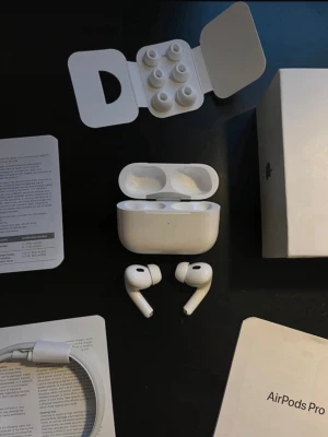 Apple AirPods Pro 2 - Säljer ett par vita Apple AirPods Pro 2 med laddningsetui och extra silikonpluggar. Hörlurarna har en stilren, kompakt design och levereras med originalkartong, laddningskabel och manual. Perfekta för musik, samtal och träning tack vare sin smidiga in-ear passform.