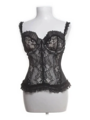Svart spetskorsett med volangdetaljer - Snygg svart korsett med spets och volangdetaljer. Justerbara axelband med små volanger. Dekorativa knappar och vacker passform som framhäver midjan.