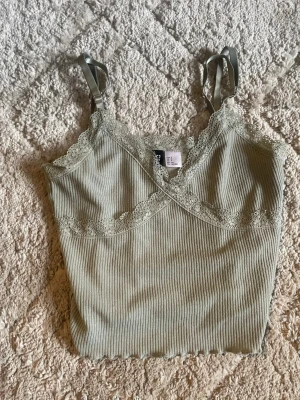 Ljusgrön ribbad linnetopp H&M Divided - Supersöt ljusgrön ribbad linnetopp från H&M Divided med spetsdetaljer längs ringningen och tunna axelband. Perfekt att styla med jeans eller kjol för en chill look. Materialet är mjukt och stretchigt för extra komfort.