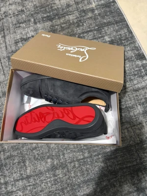 Svarta mocka sneakers från Louboutin - Säljer ett par svarta sneakers från Christian Louboutin i mjuk mocka. Skorna har klassisk snörning, rund tå och den ikoniska röda sulan. Perfekta för dig som vill ha en clean och lyxig look med en twist. Kommer i originalkartong.