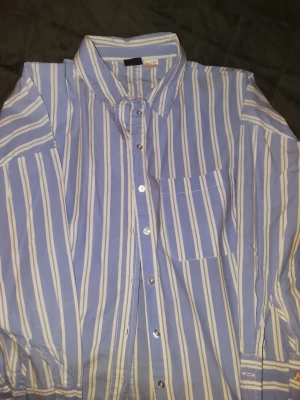 Blåvit randig skjorta Gina Tricot - Säljer en blå och vit randig skjorta från Gina Tricot. Skjortan har klassisk krage, bröstficka och knappar framtill. Tillverkad i mjuk bomull och har långa ärmar med knapp vid manschetten. Perfekt för en avslappnad och trendig look.