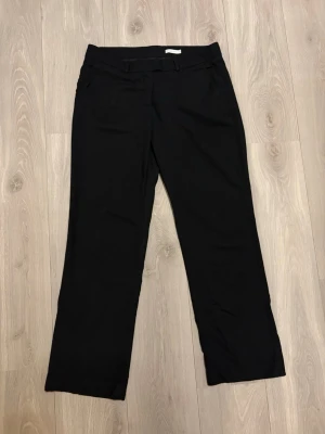 Vintage Svarta kostymbyxor från Stockh LM - Klassiska svarta kostymbyxor från Stockh LM med raka ben och hällor för bälte. Byxorna har en stilren design och är perfekta för en dressad look. Tillverkade i ett mjukt och följsamt material som ger en snygg passform. Passar mig som har 32/32