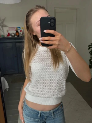 Vit stickad kortärmad tröja - Snygg vit stickad tröja med korta ärmar och rund hals. Tröjan har ett luftigt hålmönster och ribbade kanter vid ärmslut och midja. Perfekt att styla med jeans för en fräsch look.