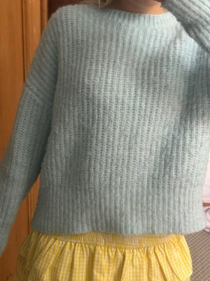 Ljusblå stickad tröja - Mysig ljusblå stickad tröja med bred ribbstickning och rund hals. Tröjan har långa ärmar och en avslappnad passform. Materialet känns fluffigt och mjukt, troligen en mohair- eller ullmix. Perfekt för lager på lager under kyliga dagar.
