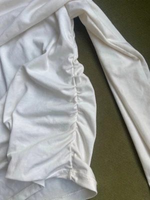 Vit långärmad topp från H&M - Säljer en vit långärmad topp från H&M med snygg rynkdetalj på sidan. Tillverkad i mjuk bomull som känns skön mot huden. Perfekt att styla med jeans eller kjol för en clean look.
