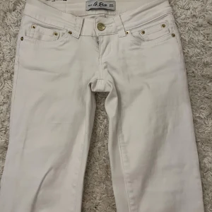 Vita bootcut jeans med gulddetaljer - Snygga vita jeans från G. Rise med bootcut passform och guldfärgade nitar vid fickorna. Jeansen har klassisk femficksdesign, gylf med knapp och dekorativa detaljer på bakfickorna. Använt 1 gång, Innerbenslängd- 77 cm