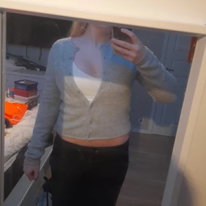 Grå stickad kofta från Gina Tricot - Supermjuk och mysig ljusgrå stickad kofta från Gina Tricot. Croppad modell med långa ärmar och knappar framtill. Perfekt att slänga över ett linne eller t-shirt för en chill look. Använd 3 gånger