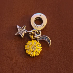 Pandora charm sol, måne & stjärna - Superfin Pandora charm i äkta silver med detaljer i guld och glittriga stenar. Hängena föreställer en stjärna, en guldfärgad sol och en måne med blå stenar. Perfekt att sätta på armband för en unik look.