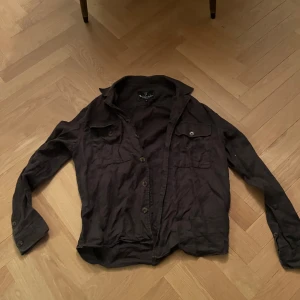 Archive mörkbrun overshirt från Bondelid - Mörkbrun skjorta från Bondelid i linne med klassisk krage, två bröstfickor med knappar och långa ärmar. Skjortan har en avslappnad passform och snygga detaljer som ger en stilren look.