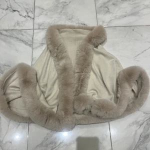 Beige pälsväst med fluffiga kanter - Supermjuk beige pälsväst med breda, fluffiga kanter i ljusbrun fuskpäls. Västen har en öppen design utan knäppning och ger en lyxig och cozy vibe. Perfekt för lager-på-lager och att lyfta vilken outfit som helst. Obs: fuskpäls men obeskrivligt len 