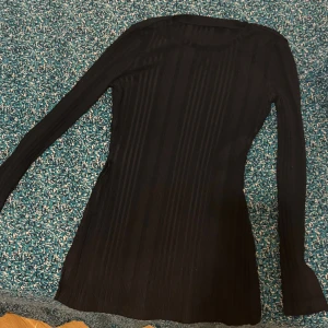 Svart ribbad långärmad topp Shein - Svart långärmad topp från Shein i storlek S. Modellen är ribbad med vertikala ränder och har en slits på sidan. Tunn och stretchig, perfekt att styla med jeans eller kjol. Enkel och clean look med rund halsringning.