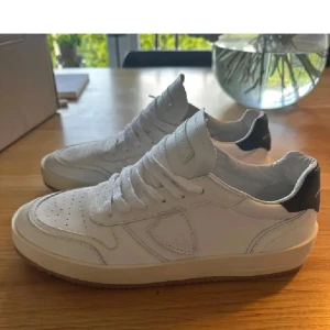 Vita Philippe Model sneakers i skinn - Snygga vita sneakers från Philippe Model i skinn med svarta detaljer på hälen. Klassisk låg modell med perforerad tå, rund tå och snörning. Perfekta för dig som gillar stilrena och trendiga skor med premiumkänsla.