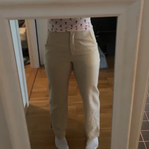 Beiga kostymbyxor med rak passform - Snygga beiga kostymbyxor med hög midja och raka ben. Byxorna har diskreta fickor och stängs med dragkedja och knapp framtill. Perfekta för en clean och stilren look. Materialet känns mjukt och bekvämt mot huden.