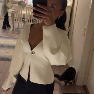 Vit v-ringad topp från Gina Tricot - Säljer en stilren vit topp från Gina Tricot i stickat material. Använd en gång. Toppen har v-ringning med en snygg guldknapp framtill. Passformen är normal och modellen är väldigt fint croppad. Skriv för fler bilder eller funderingar❤️