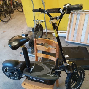 Gyroway elscooter - Stabil Gyroway elscooter med sadel, grova däck och fjädring. Batteriluckan visar kablage och batterier, allt ser komplett ut. Viss yttre smuts och normalt bruksslitage, den ända synliga skadan är bromsarna. Perfekt för pendling eller fritid. Kör i 32km/h