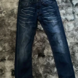 Smog denim jeans - Snygga mörkblå jeans från Smog Denim med slitna detaljer och kontrastsömmar. Klassisk femficksmodell med coola ljusa tvättade partier framtill. Perfekta för dig som gillar en avslappnad men trendig look. Storlek 30/32
