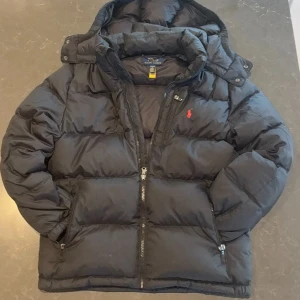 Svart pufferjacka från Polo Ralph Lauren - Säljer en stilren svart pufferjacka från Polo Ralph Lauren i storleken L barn. Det är ett perfekt plagg nu när de kalla vädret börjar komma fram. Om det är något är det bara att fråga🙌