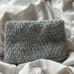 Grå virkad necessär med dragkedja - Handgjord grå necessär i virkat garn med ett snyggt blommigt mönster. Väskan har vit dragkedja och är fodrad med grått tyg med små prickar. Perfekt för att bära småsaker eller använda som sminkväska.