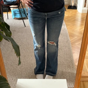 Blå flare jeans från H&M, storlek 27/30 - Snygga blå jeans från H&M i flare-modell med regular waist. Jeansen har slitna detaljer och hål på benen för en trendig look. Tillverkade i klassiskt denimtyg och har råa kanter nertill. Perfekta för dig som gillar en avslappnad och cool stil.