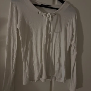 Vit ribbad långärmad tröja med snörning - Säljer en vit långärmad tröja med ribbad struktur och snygg snörning vid halsen. Tröjan har en enkel och clean look med mjukt material som känns skönt mot huden. Perfekt för dig som gillar stilrena och bekväma plagg.