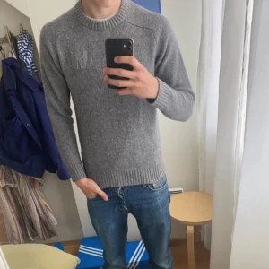 stickad tröja - Säljer en grå stickad tröja från Wood Wood i storlek small. Perfekt för dig som gillar enkel och clean stil med snygga detaljer. Använd ett par gånger bara, dock sitter lappen i kragen lite löst men inget som märks.