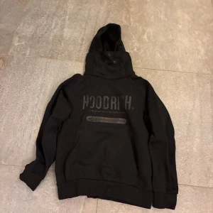 Svart hoodie från Hoodrich - Svart hoodie från Hoodrich med stor logga på bröstet och praktisk ficka med dragkedja framtill. Tröjan har huva med snörning och långa ärmar, perfekt för en chill och street-inspirerad look 1000kr nypris ungefär från london.