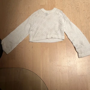 Vit croppad stickad tröja Divided - Säljer en vit croppad stickad tröja från Divided, H&M. Tröjan har ett snyggt hålmönster och långa ärmar med ribbade muddar. Perfekt för dig som gillar en chill och trendig stil. Passar till både jeans och kjol.