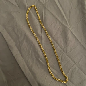 Guldtonat tvinnat halsband - Snyggt halsband med tvinnad kedja i guldtonad metall. Kedjan har en robust karbinlås och glänsande finish som ger en cool och modern vibe. Perfekt för att lyfta din stil med en enkel men iögonfallande detalj.