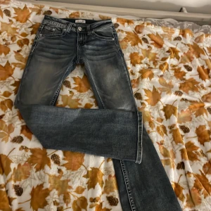 Fire & Rain blå jeans med broderi - Snygga blå jeans från Fire & Rain med coola broderade kors på bakfickorna och nitar längs fickkanterna. Jeansen har en klassisk femficksdesign, kontrastsömmar och en lätt tvättad look. Passar dig som gillar detaljer och unik stil.