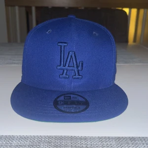  LA Dodgers keps från New Era - Säljer en blå snapback keps från New Era med LA Dodgers brodyr framtill och flera broderade märken på sidan. Baktill står det '6X CHAMPS' i vitt. Klassisk platt skärm och justerbar passform. Perfekt för dig som gillar sportig stil och vill sticka ut.