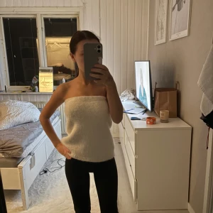Vit stickad tubtopp - Säljer en supermjuk och fluffig vit stickad tubtopp. Toppen är axelbandslös och har en enkel, rak form som sitter snyggt över överkroppen. Perfekt för dig som gillar minimalistisk stil och vill ha något bekvämt men ändå trendigt.
