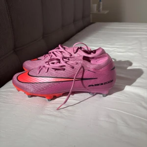 Nike Air Zoom rosa fotbollsskor - Säljer ett par Nike Air Zoom fotbollsskor i en riktigt snygg rosa färg med neonrosa detaljer och svarta swoosh-loggor. Skorna har snörning och metall-dobbar för bästa grepp på planen. Lätta och smidiga med syntetmaterial som ger en modern look.