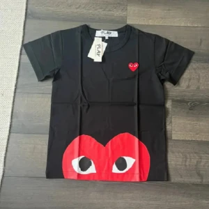 Cdg t shirt - Helt ny Svart t-shirt från Comme des Garçons Play med ikoniskt rött hjärta med ögon på bröstet och stor röd hjärtdetalj med ögon längst ner. Klassisk rund hals och korta ärmar. Tillverkad i mjuk bomull för en skön känsla.