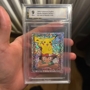 1999 Pokémon English Merlin Stickers Series 1 S2 Ash & Pikachu Holo - Samlarstickers med holografisk effekt från Pokémon, featuring Ash och Pikachu. Perfekt för dig som älskar nostalgi och vill ha något unikt i din samling. Graderad Mint 9 och skyddad i plastfodral. Ett måste för Pokémon-fans!