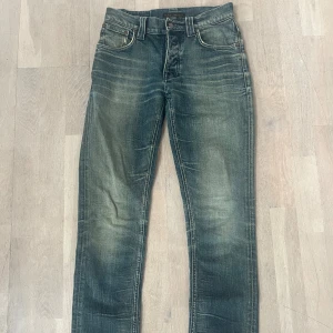 Nudie Jeans blå jeans W30 L32 - Snygga blå jeans från Nudie Jeans med klassisk femficksdesign och slitna detaljer. Jeansen har raka ben modell Grim Tim. Något liten i storlek mer W29. 