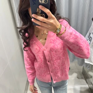 Rosa Hello Kitty kofta från H&M x Sanrio - Supergullig rosa kofta från H&M x Sanrio med Hello Kitty-mönster över hela tröjan. Koftan har v-ringning, knappar framtill och ribbade muddar. Perfekt för dig som älskar söta detaljer och vill sticka ut lite extra.