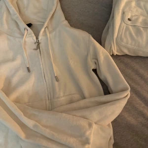 Vitt mjukis set från Juicy Couture - Säljer ett par vita mjukisbyxor och tröja från Juicy Couture med bred resår i midjan och snörning med silverdetaljer. Byxorna har stora fickor fram och bak med knappar, samt broderad logga på fickan. Materialet är mjukt och skönt, perfekt för chill.