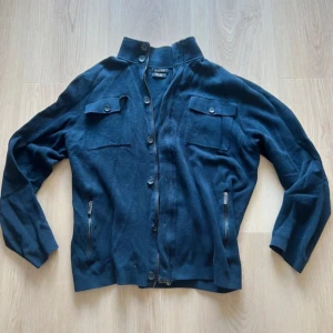 Mörkblå stickad overshirt Massimo Dutti - Snygg mörkblå stickad overshirt från Massimo Dutti i bomull. Jackan har ståkrage med knappar, två bröstfickor med lock, dragkedjor vid sidorna och knappstängning framtill. Perfekt för dig som gillar stilrena detaljer och en chill look.