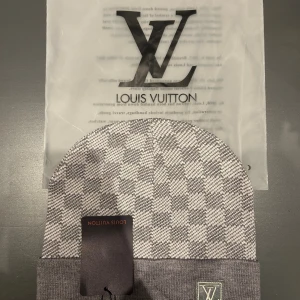 Grå rutig  mössa - Snygg grå och vit rutig mössa från  med klassisk logga broderad framtill på uppviket. Mössan är stickad och har en mjuk, skön känsla som passar perfekt när det är kallt ute. Den rutiga designen ger en trendig och exklusiv vibe.