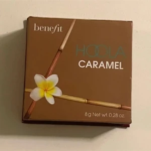 Benefit Hoola Caramel Bronzer - Säljer en Benefit Hoola Caramel bronzer i en snygg brun kartong med spegel i locket. Pudret har en varm karamellbrun nyans och är pressat i fyrkantig form. Perfekt för att skapa en solkysst look och contoura ansiktet.